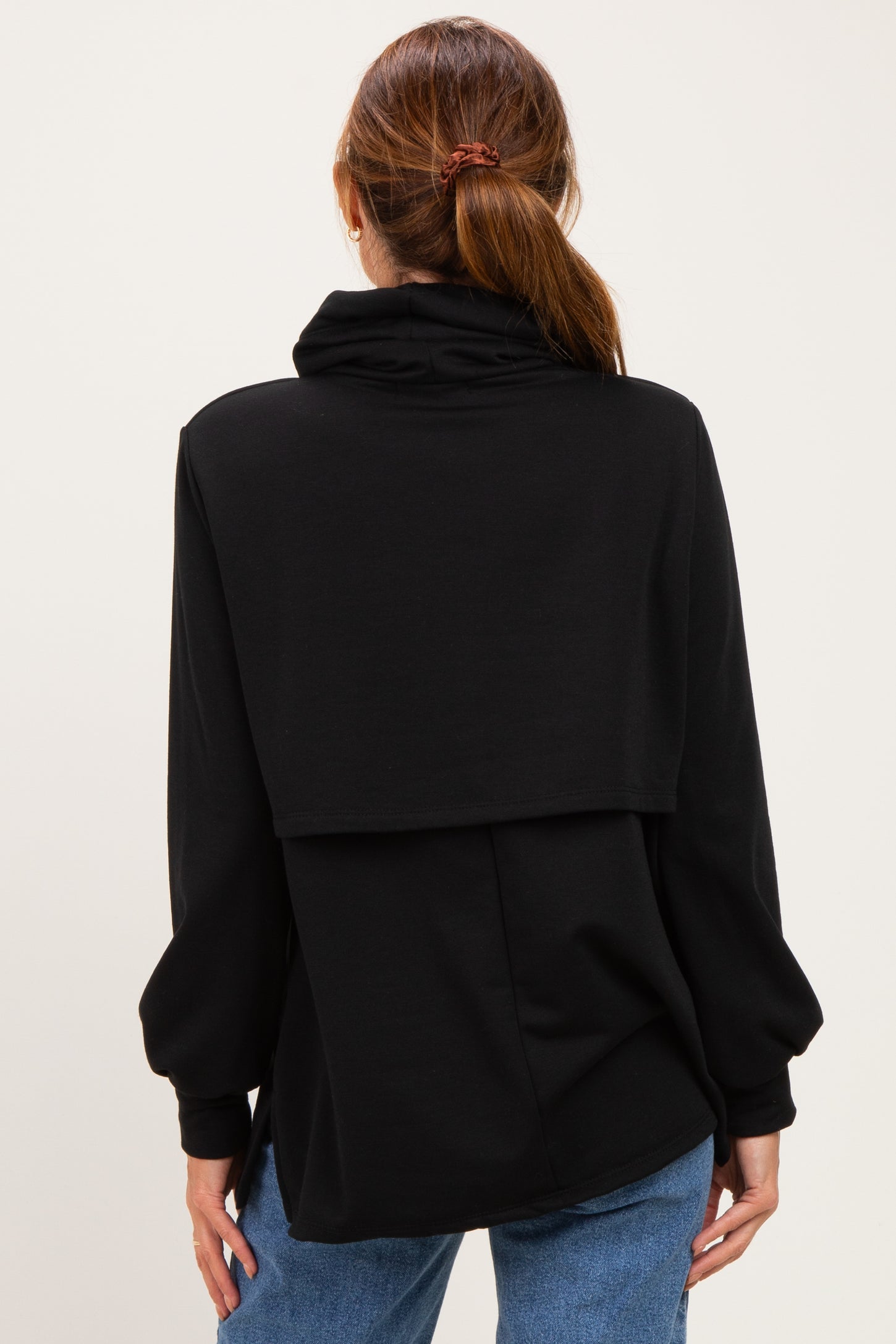 woman wearing a black oversized sweatshirt with a cowl neck and long sleeves, facing away from the camera