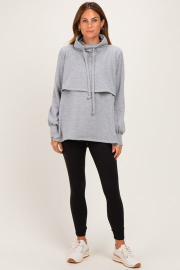 woman wearing a gray cowl neck oversized sweatshirt layered over a long sleeve top with black leggings and sneakers