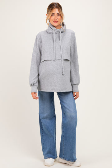 woman wearing a gray cropped maternity hoodie with a drawstring and paired with wide-leg jeans, showing a baby bump