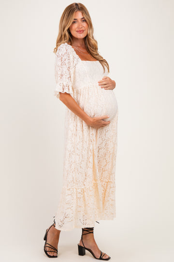 woman wearing a cream lace maternity dress with short sleeves and holding her baby bump