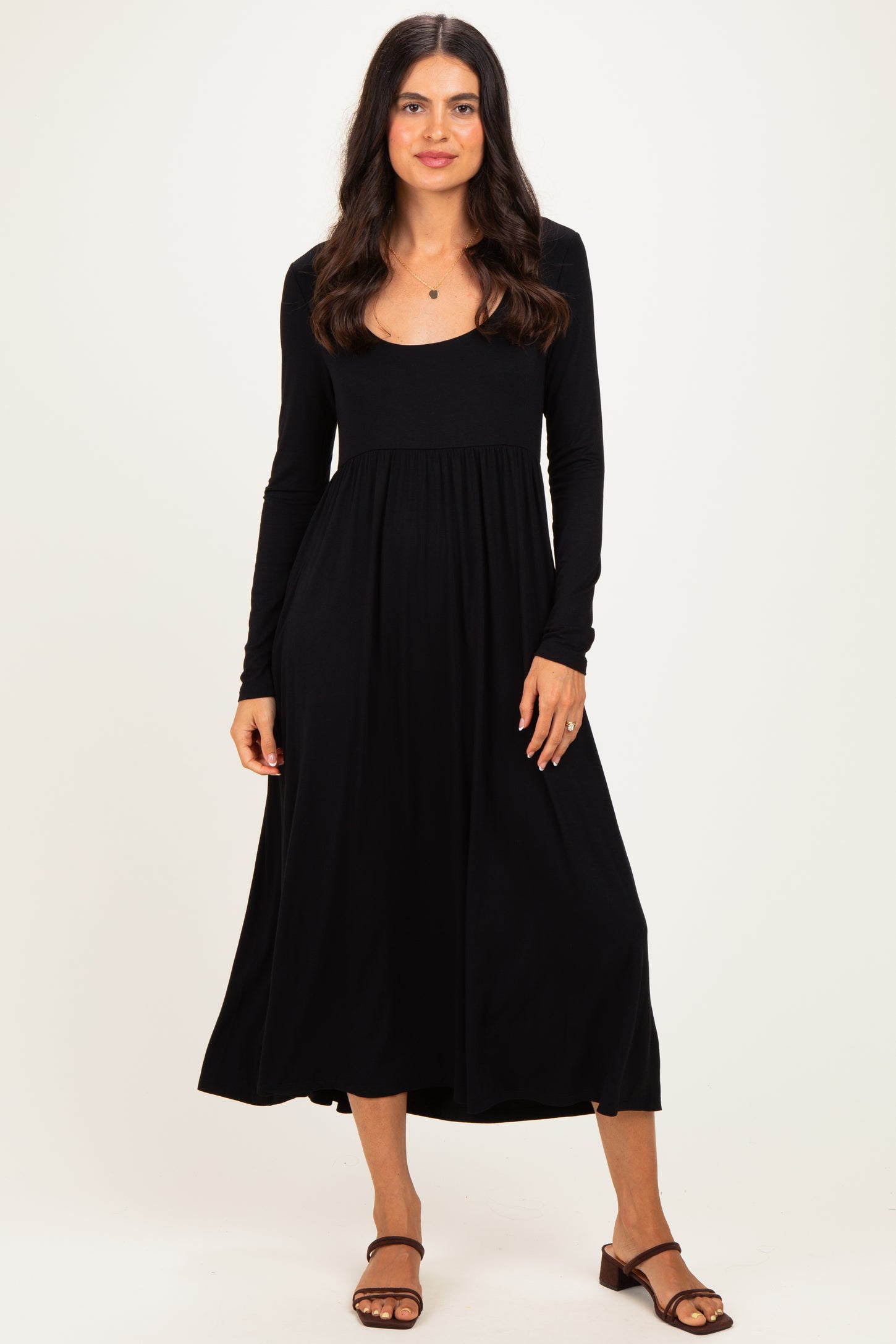 woman wearing a black long sleeve midi dress with a fitted bodice and flowing skirt, standing on a plain background