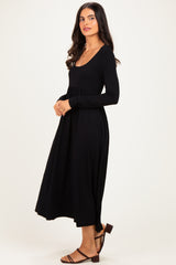 woman wearing a black long sleeve dress with a scoop neckline and gathered waist, standing sideways