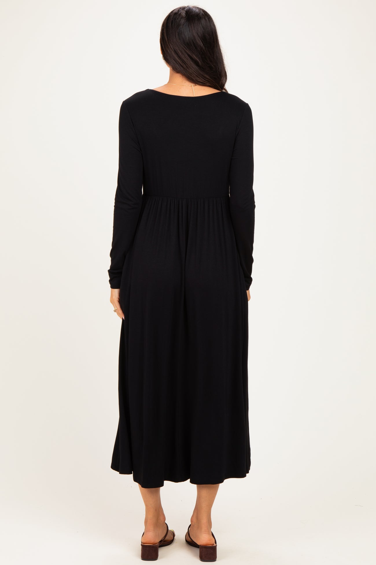woman wearing a black long sleeve maxi dress, showing a fitted bodice and flowing skirt from the back
