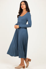 woman wearing a deep blue long sleeve maxi dress with a fitted bodice and flowing skirt, paired with beige mules