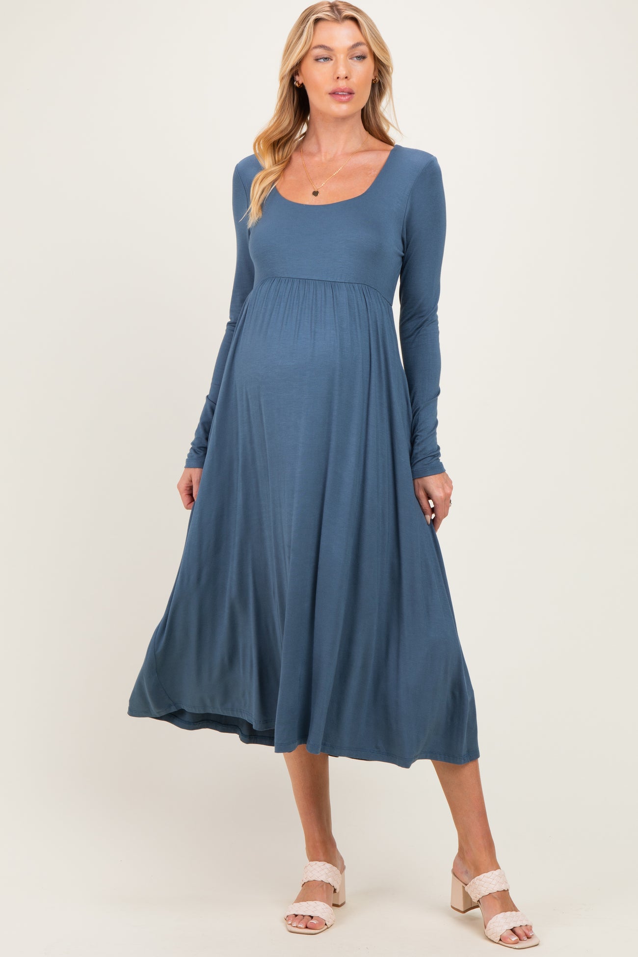 woman wearing a blue long sleeve maternity dress with a scoop neckline and flowing skirt, showing a baby bump