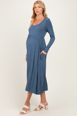 woman wearing a teal long sleeve maternity dress with side pockets and a visible baby bump