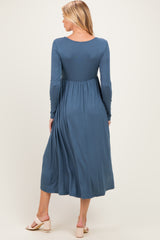 woman wearing a teal long sleeve maternity dress with a flowy skirt and a fitted bodice, seen from the back
