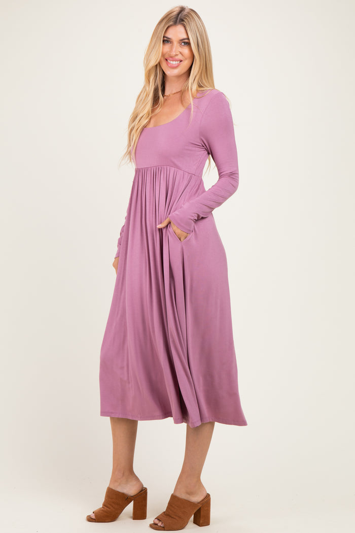 woman wearing a mauve long sleeve midi dress with a gathered waist and side pockets, paired with brown block-heeled mules
