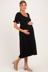 woman wearing a black maternity dress with puff sleeves and buttons, holding her baby bump
