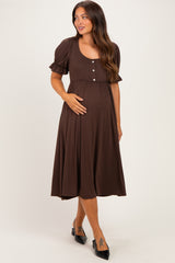 woman wearing a brown maternity dress with short puff sleeves and buttons, gently holding her baby bump