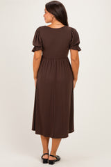 woman wearing a brown maternity dress with short puff sleeves and a cinched waist, showing a baby bump from the back