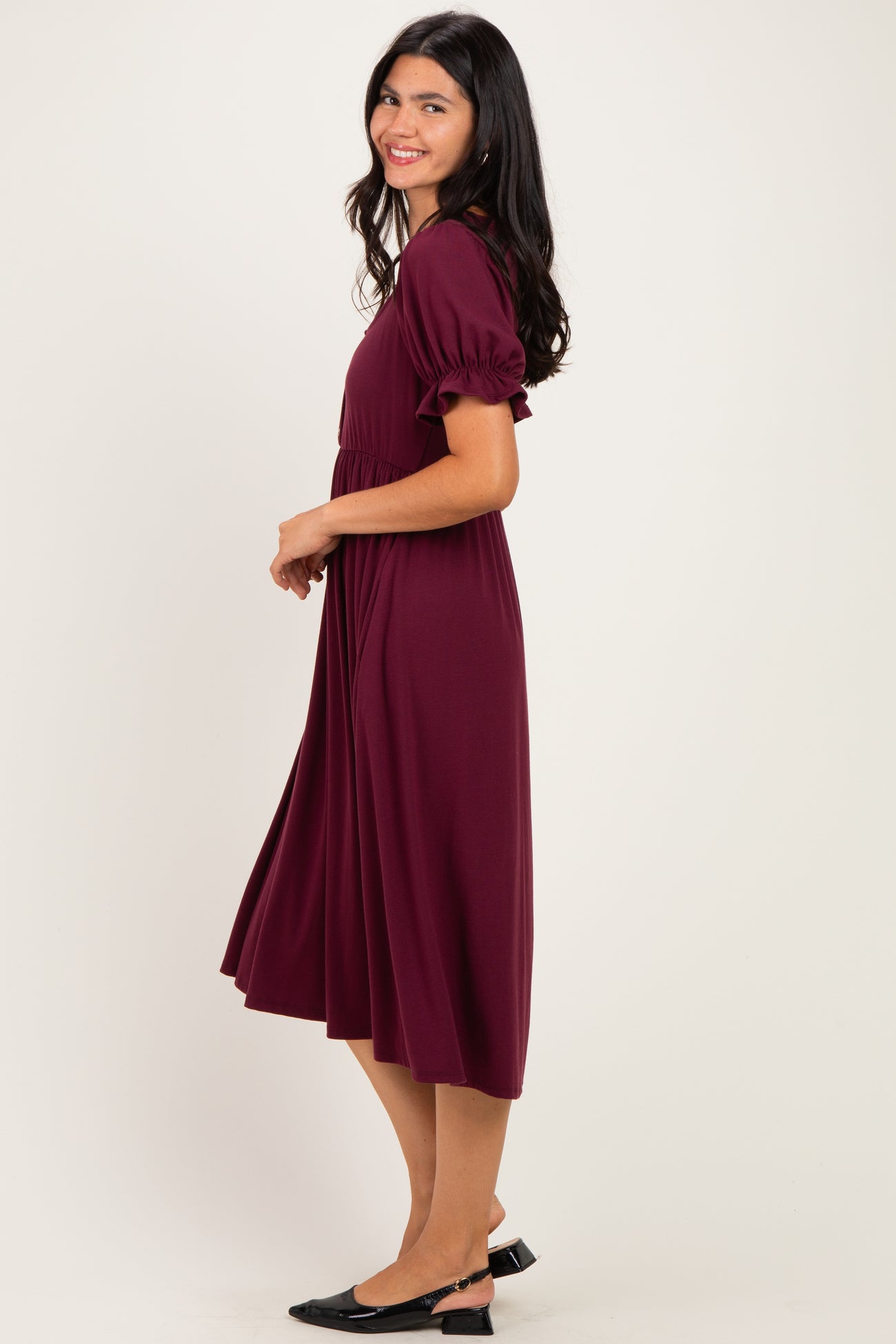 woman wearing a wine red midi dress with puff sleeves, smiling and standing sideways