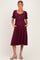 woman wearing a burgundy maternity dress with short puff sleeves, pockets, and buttons down the front, showcasing her baby bump