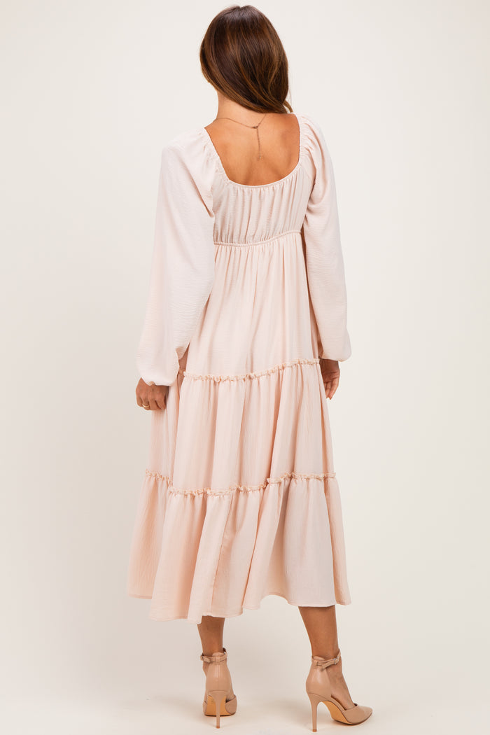 woman wearing a blush pink long sleeve tiered maxi dress, showing the back view with a scoop neckline