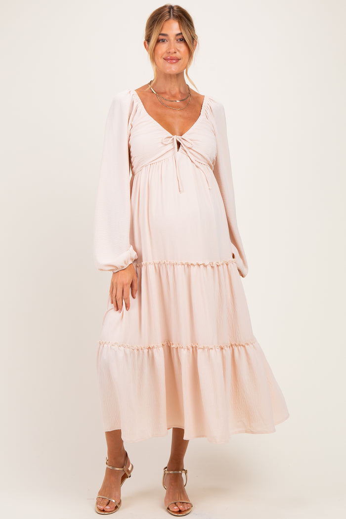 woman wearing a light pink maternity dress with a tie-front detail and tiered skirt, showcasing her baby bump