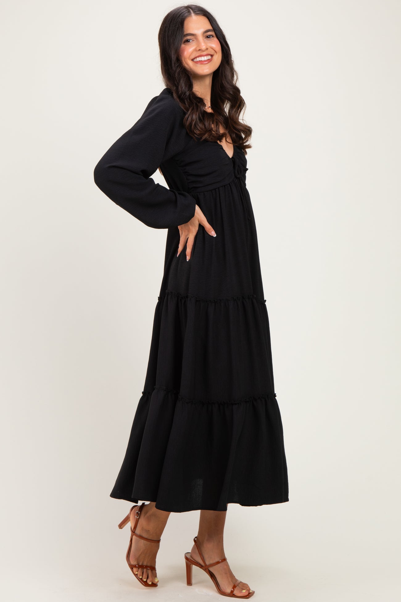 woman wearing a black tiered maxi dress with long sleeves and a fitted bodice, posing with one hand on her hip
