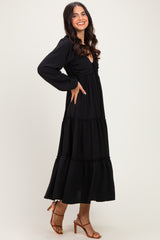 woman wearing a black tiered maxi dress with long sleeves and a fitted bodice, posing with one hand on her hip