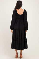 woman wearing a black long sleeve tiered dress with a backless design and puffed sleeves
