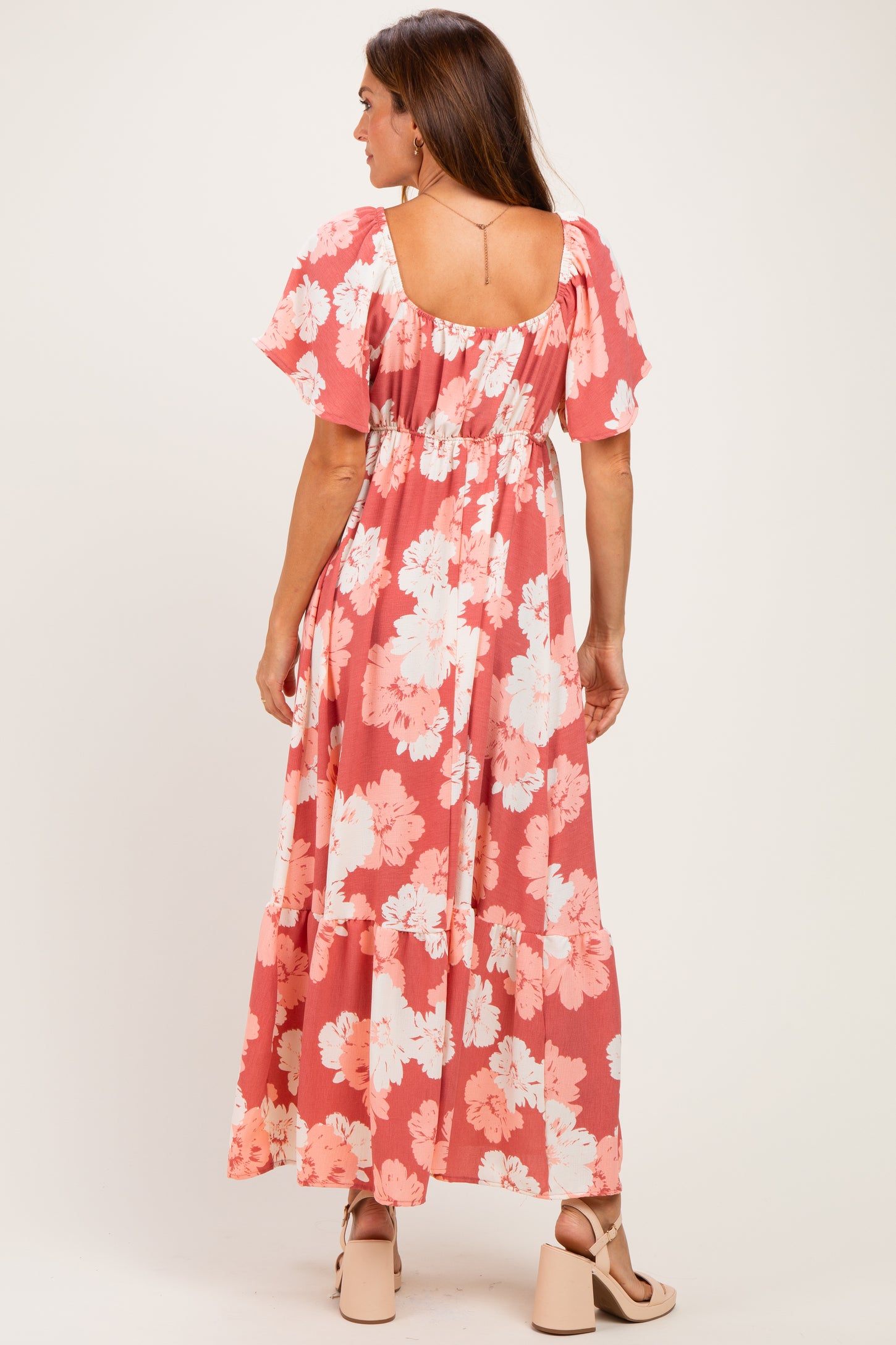 woman wearing a coral floral maxi dress with flutter sleeves and a tiered hem from the back