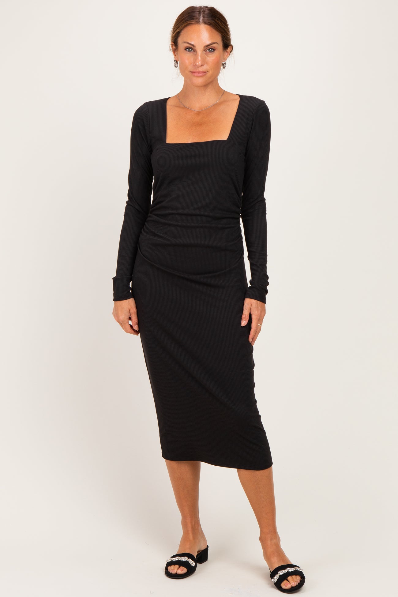 woman wearing a fitted black ribbed long sleeve dress with a square neckline and midi length, standing against a neutral background