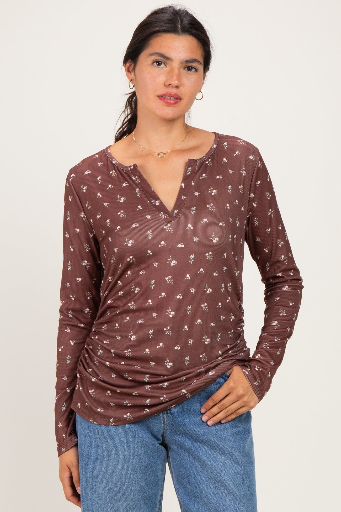 woman wearing a brown long sleeve henley top with a floral print and gathered sides, paired with light blue jeans
