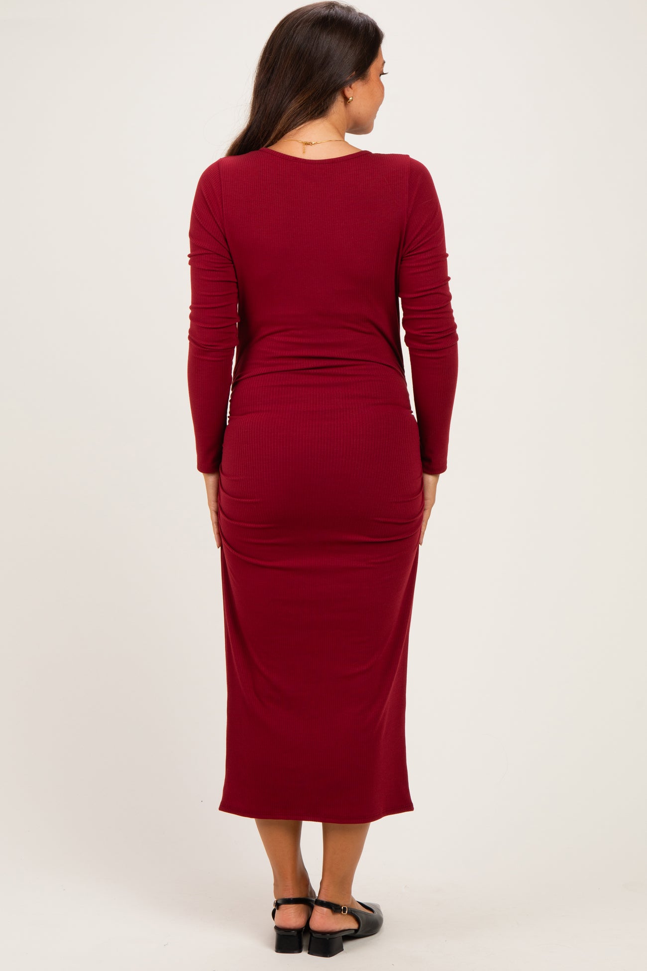 woman wearing a burgundy long sleeve maternity dress with ruching details and a fitted silhouette