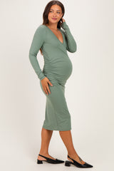 woman wearing a sage green maternity dress with long sleeves and side ruched detailing, showcasing her baby bump