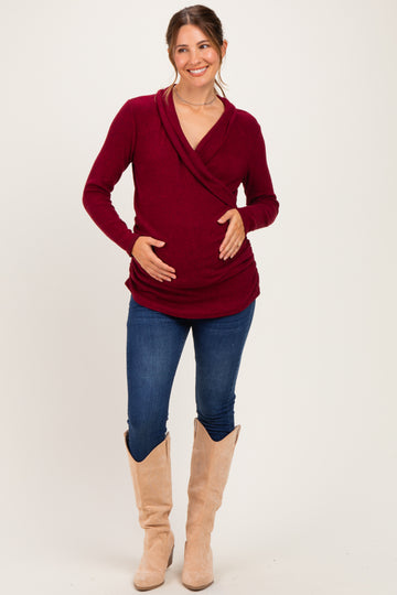 woman wearing a burgundy maternity wrap top and blue jeans, showing her baby bump, and paired with beige boots