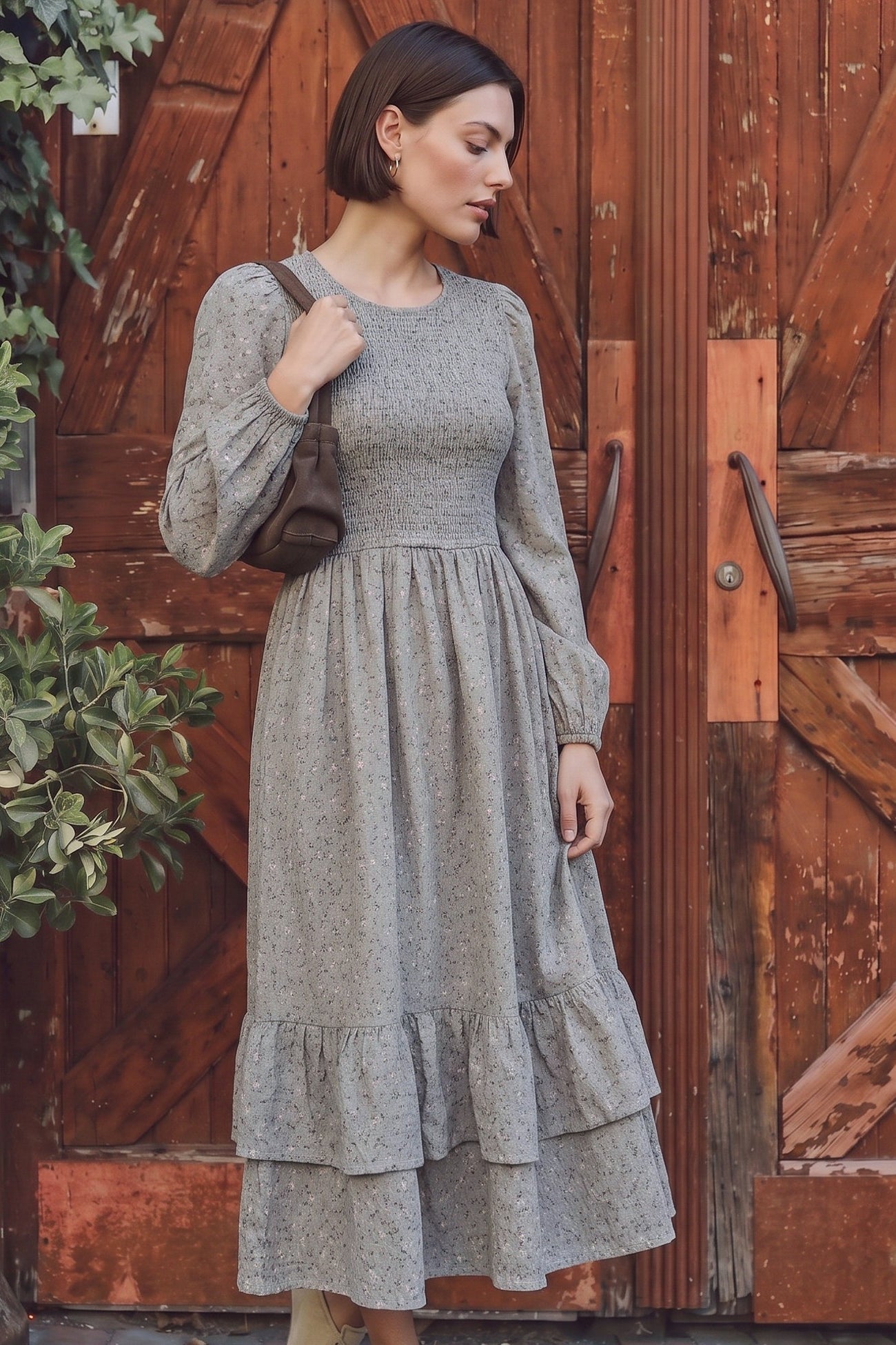 woman wearing a grey floral maxi dress with a smocked bodice and tiered ruffle hem, standing in front of wooden doors