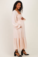 woman wearing a light pink maternity dress with a smocked bodice and long sleeves, touching her baby bump