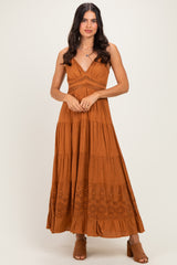 woman wearing a rust-colored maxi dress with a tiered design and eyelet details, standing with a slight pose