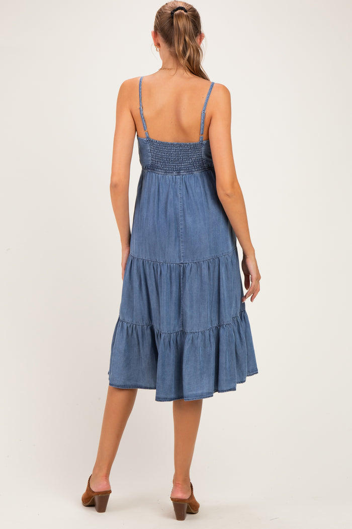 woman wearing a blue denim maternity dress with a smocked bodice and tiered skirt, showing a baby bump from behind