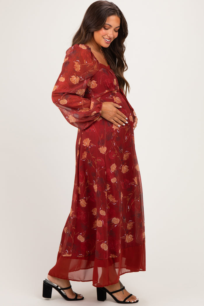 woman wearing a flowy red floral maternity maxi dress and holding her baby bump
