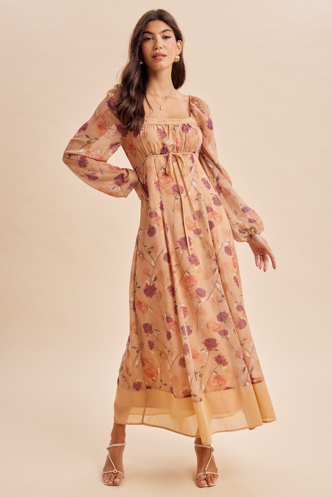 woman wearing a floral long sleeve maxi dress in beige with purple and orange flowers, featuring a square neckline and tie detail