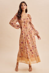 woman wearing a floral long sleeve maxi dress in beige with purple and orange flowers, featuring a square neckline and tie detail