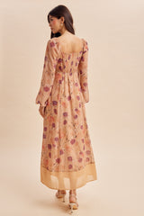woman wearing a floral maxi dress with long sleeves and a smocked back, standing against a light background