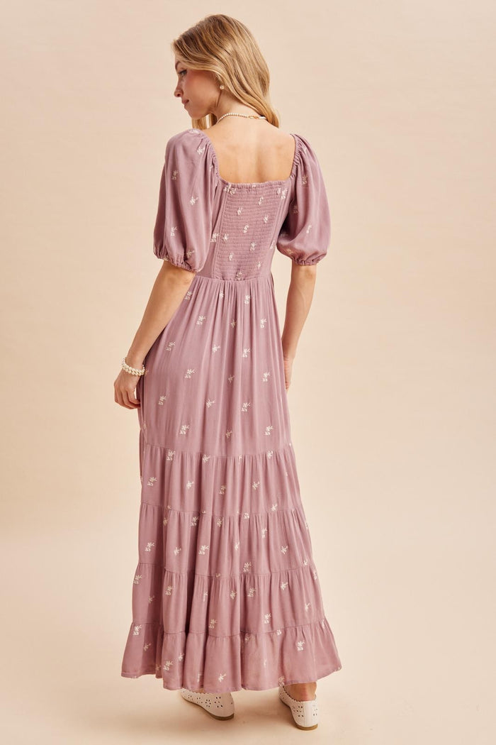 woman wearing a lilac maxi dress with puff sleeves and floral embroidery, showing the back view