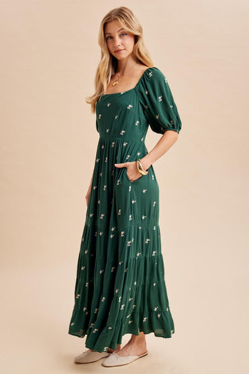 woman wearing a green floral maxi dress with puff sleeves and pockets, standing on a neutral background