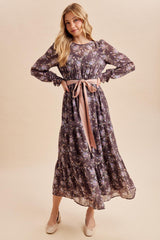 woman wearing a long sleeve dark floral maxi dress with a thigh-high slit and a pink ribbon tie at the waist