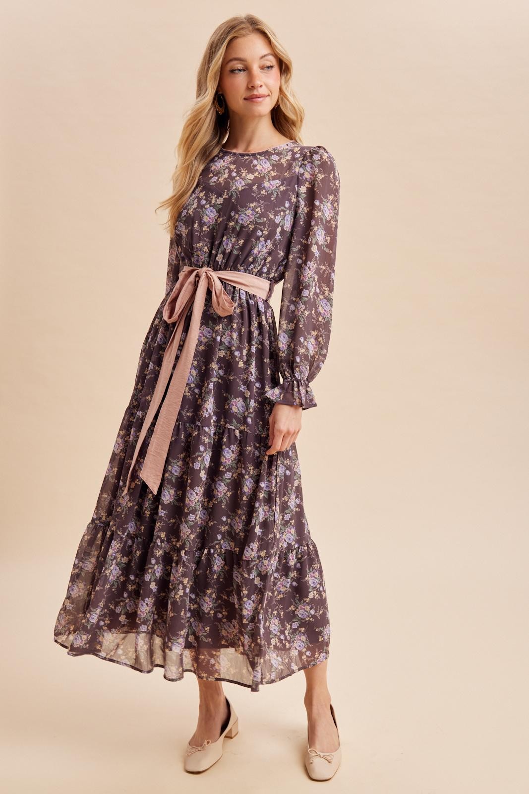 woman wearing a dark floral maxi dress with a pink tie belt and long sleeves