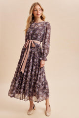 woman wearing a dark floral maxi dress with a pink tie belt and long sleeves