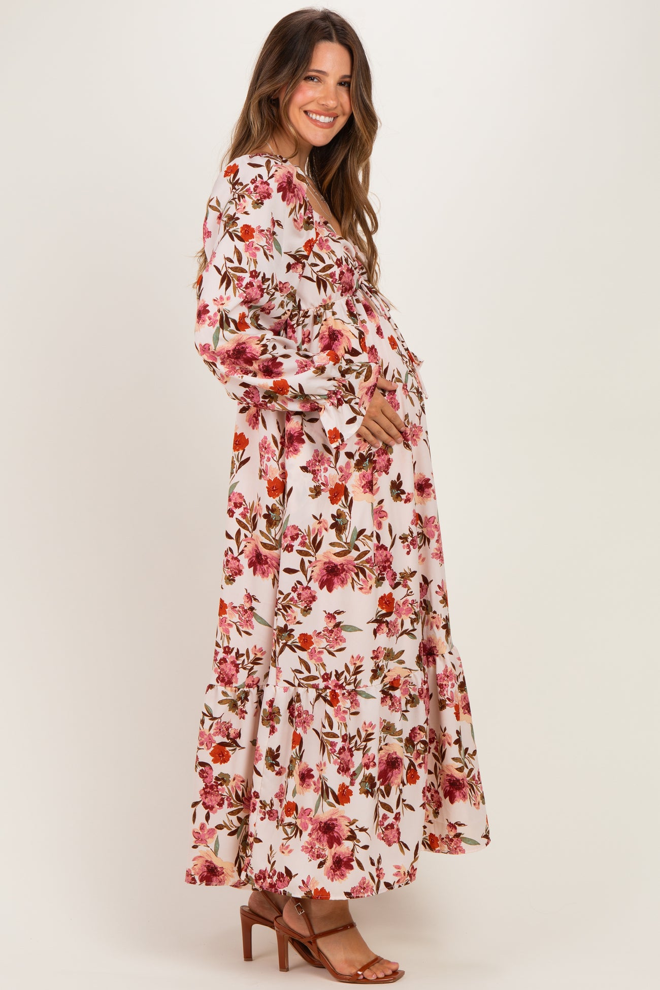 woman wearing a floral maxi maternity dress with a ruffled hem and holding her baby bump