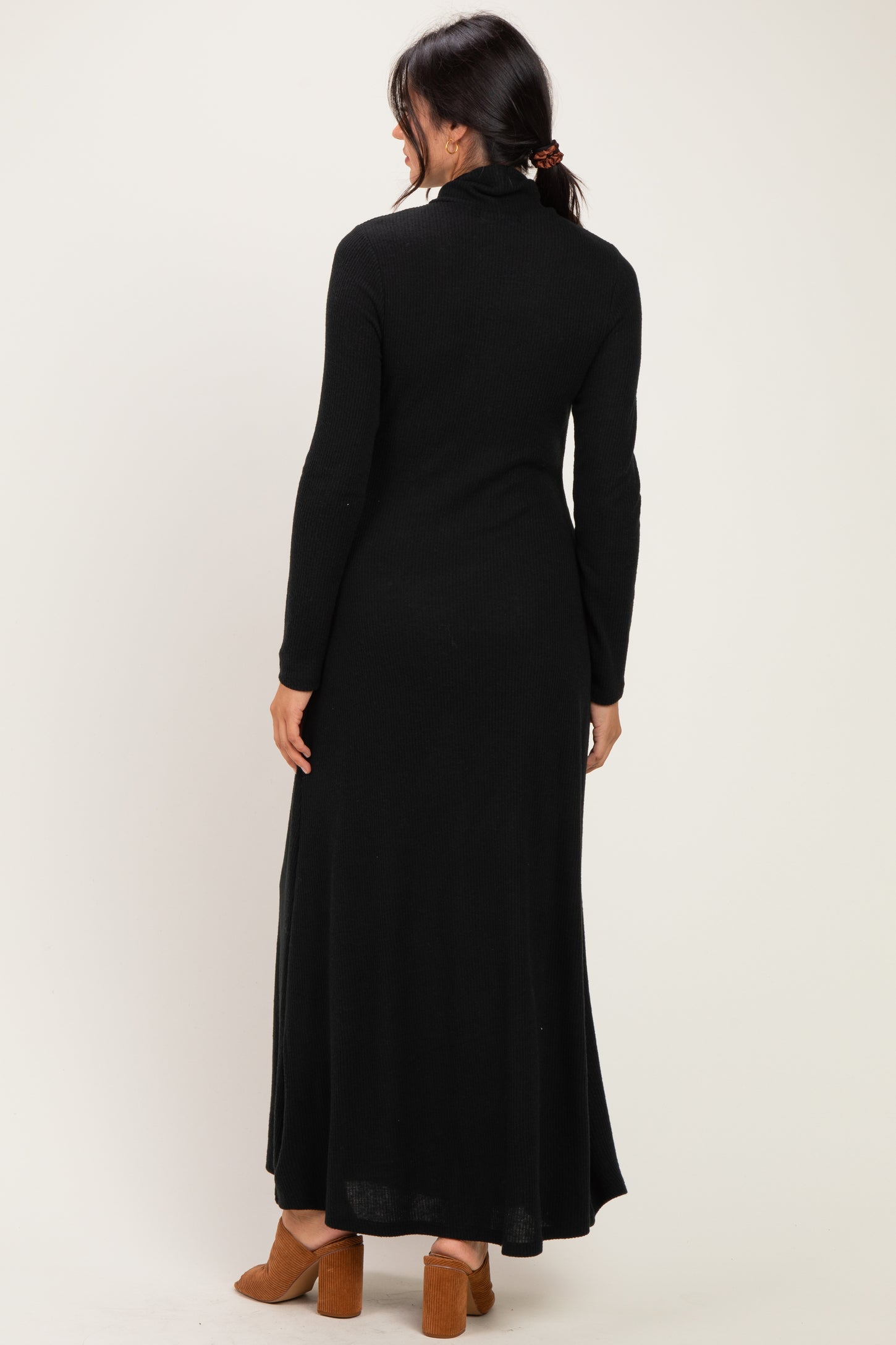 woman wearing a black long sleeve maxi dress with a high neckline and side slits, viewed from the back