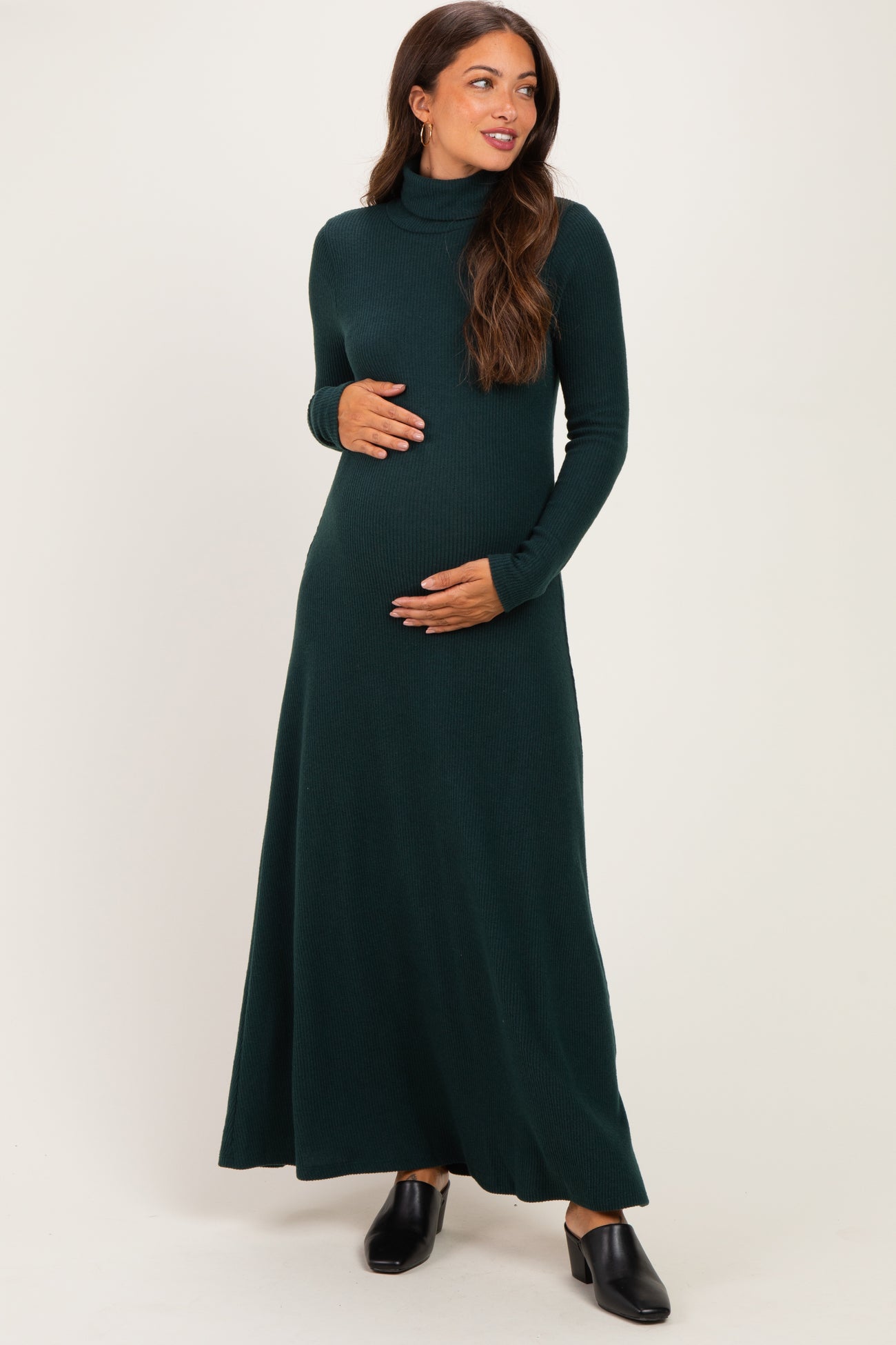woman wearing a dark green long sleeve maternity maxi dress while holding her baby bump