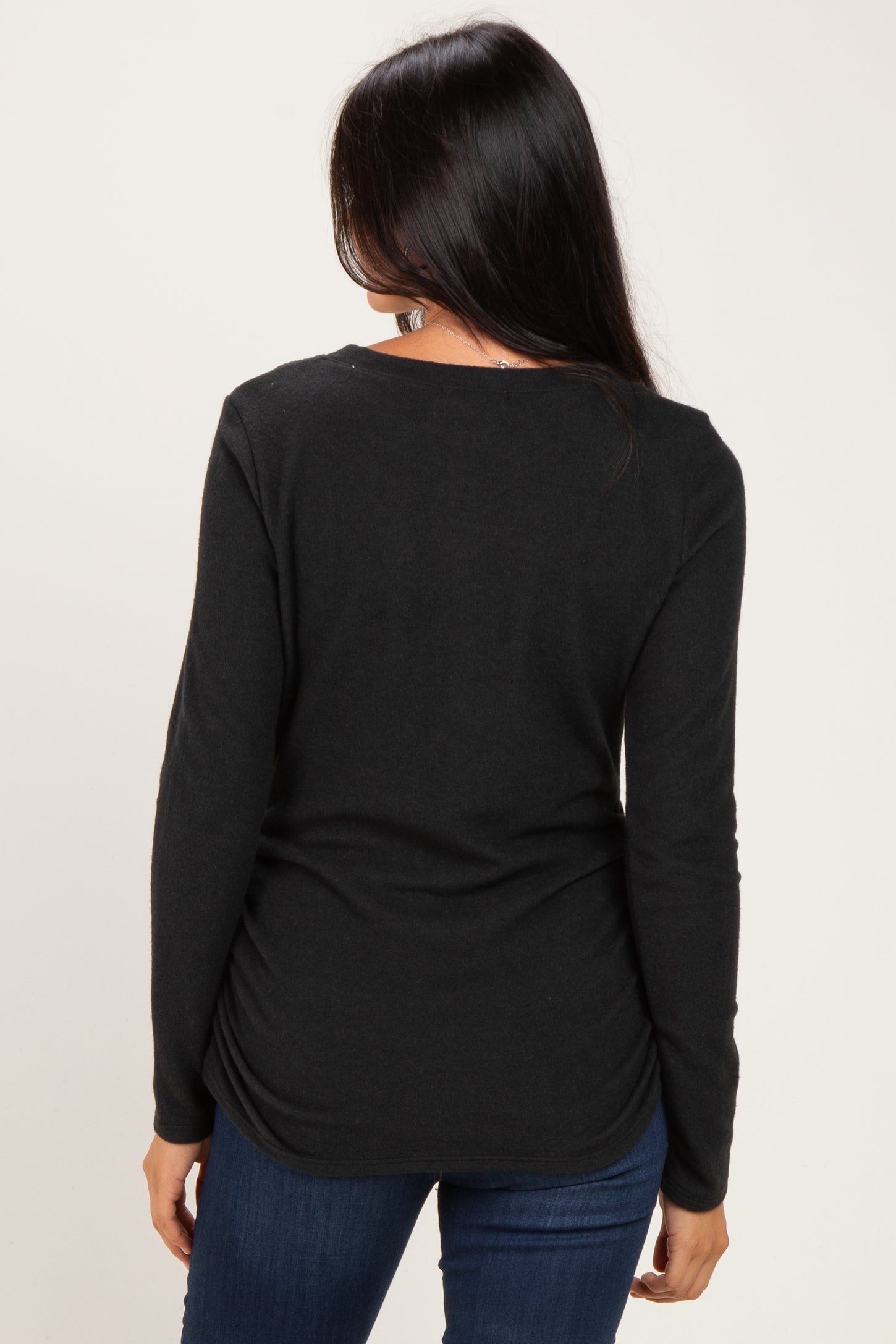 woman wearing a black long sleeve top with a scoop neck and gathered back detail, paired with blue jeans