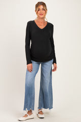 woman wearing a black v-neck maternity top and light blue wide-leg jeans, showing her baby bump