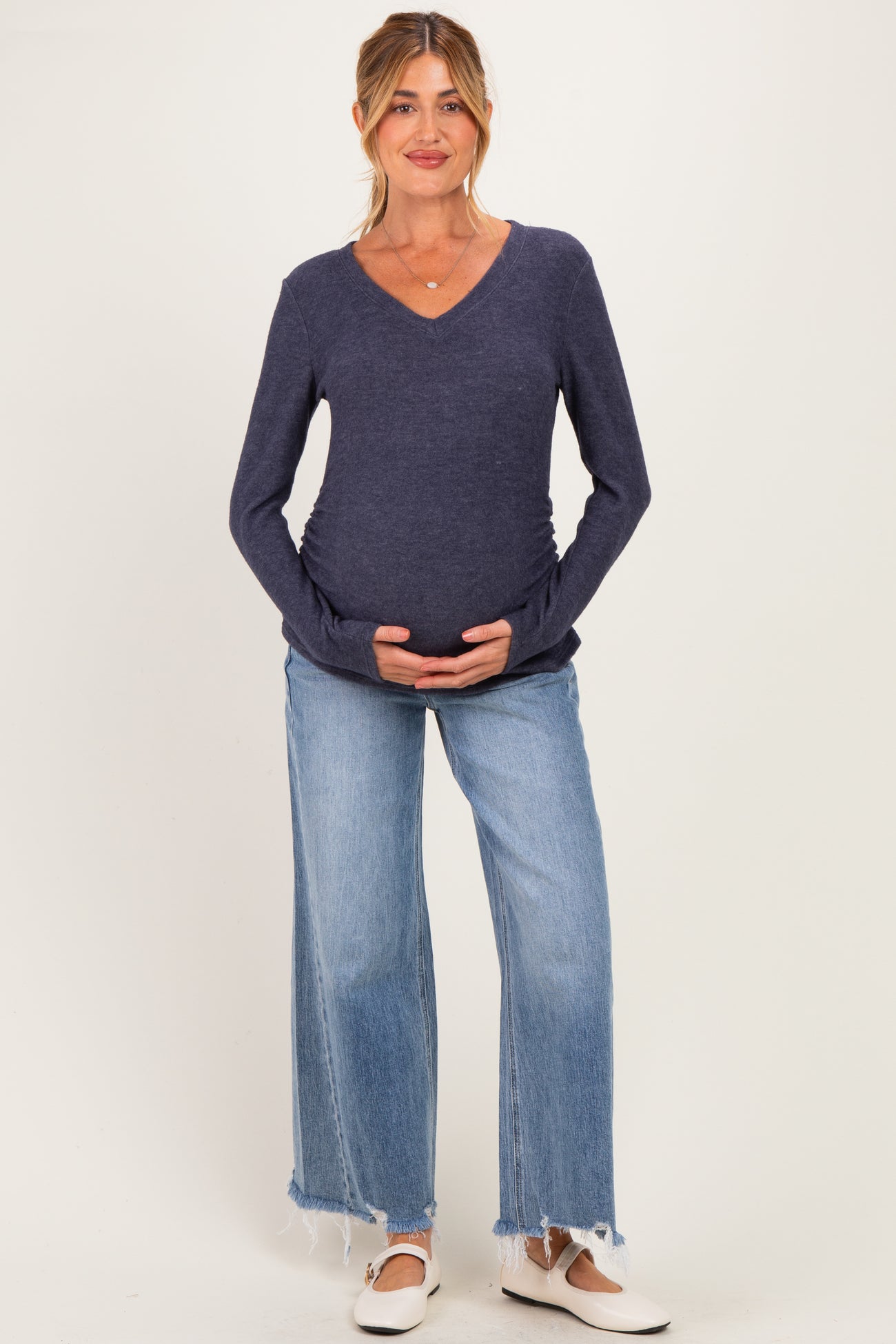 woman wearing a navy maternity v-neck sweater and blue wide-leg jeans, gently holding her baby bump