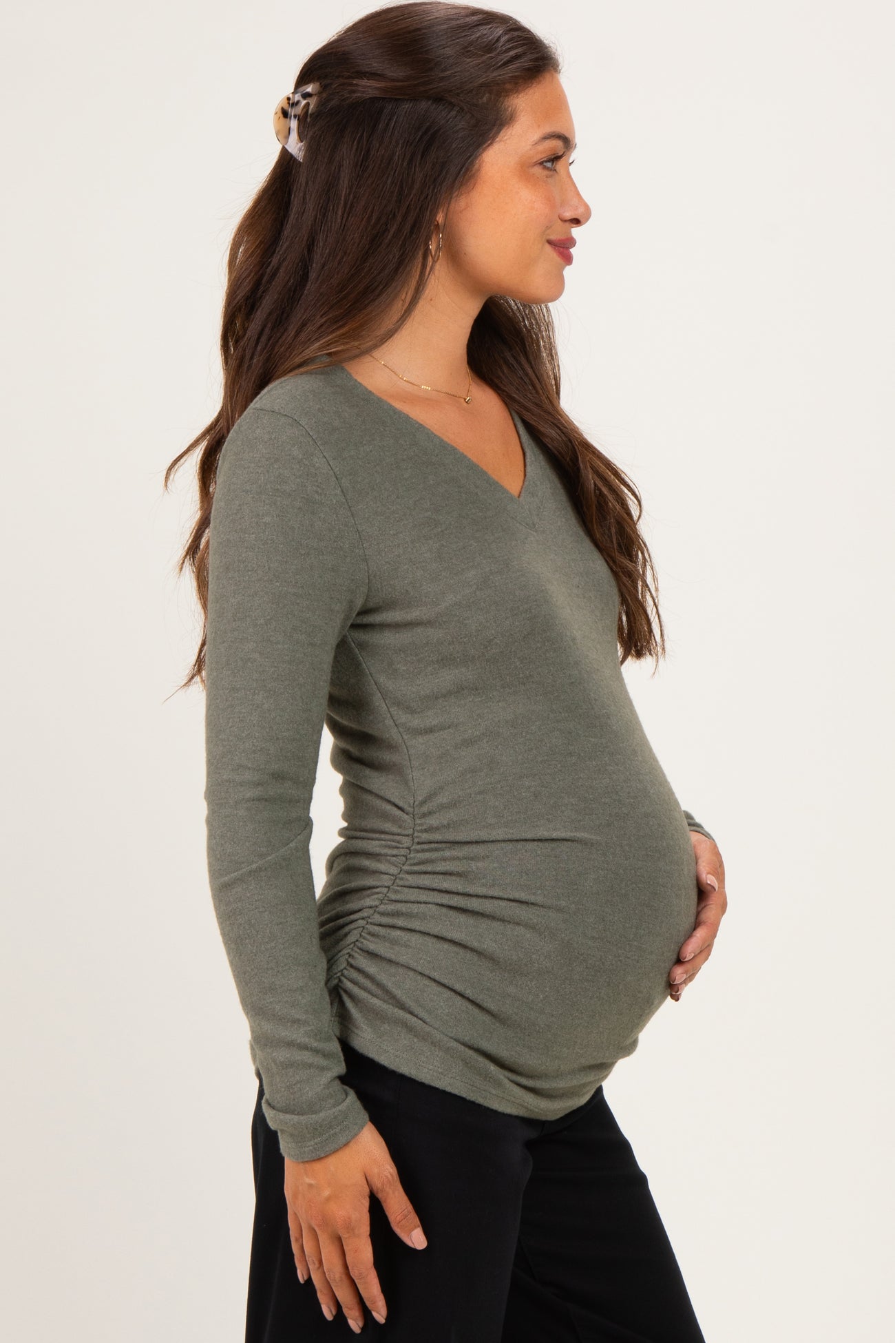 woman wearing an olive green long sleeve maternity top with side ruching and showing her baby bump