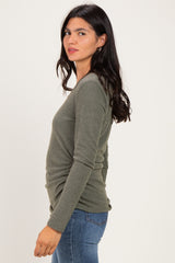 woman wearing an olive green long sleeve top with a ruched side detail and styled with blue jeans