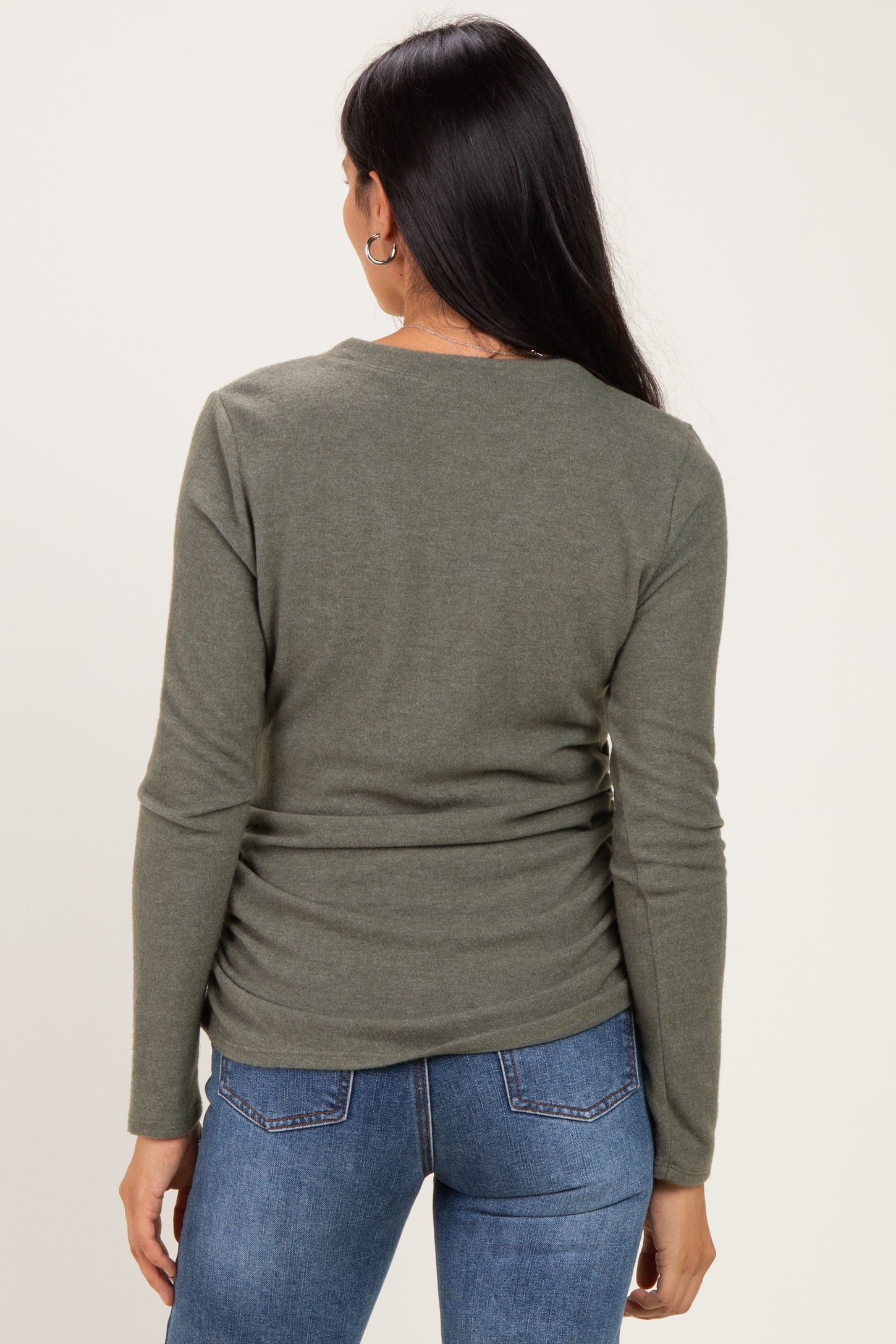 woman wearing a dark green long sleeve top with a fitted design, viewed from the back with blue jeans.